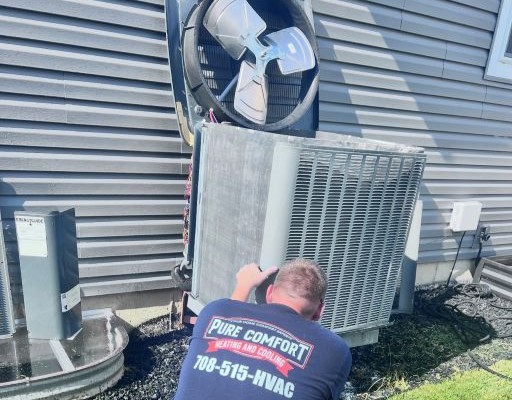 Pure Comfort technician servicing an outdoor air conditioner with the top and coil exposed