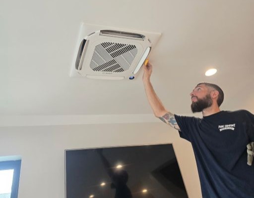Pure Comfort technician servicing a Bosch ceiling-cassette mini-split in a finished living room