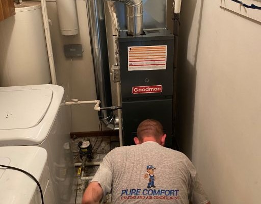Pure Comfort technician installing a Goodman gas furnace in a laundry-room mechanical closet