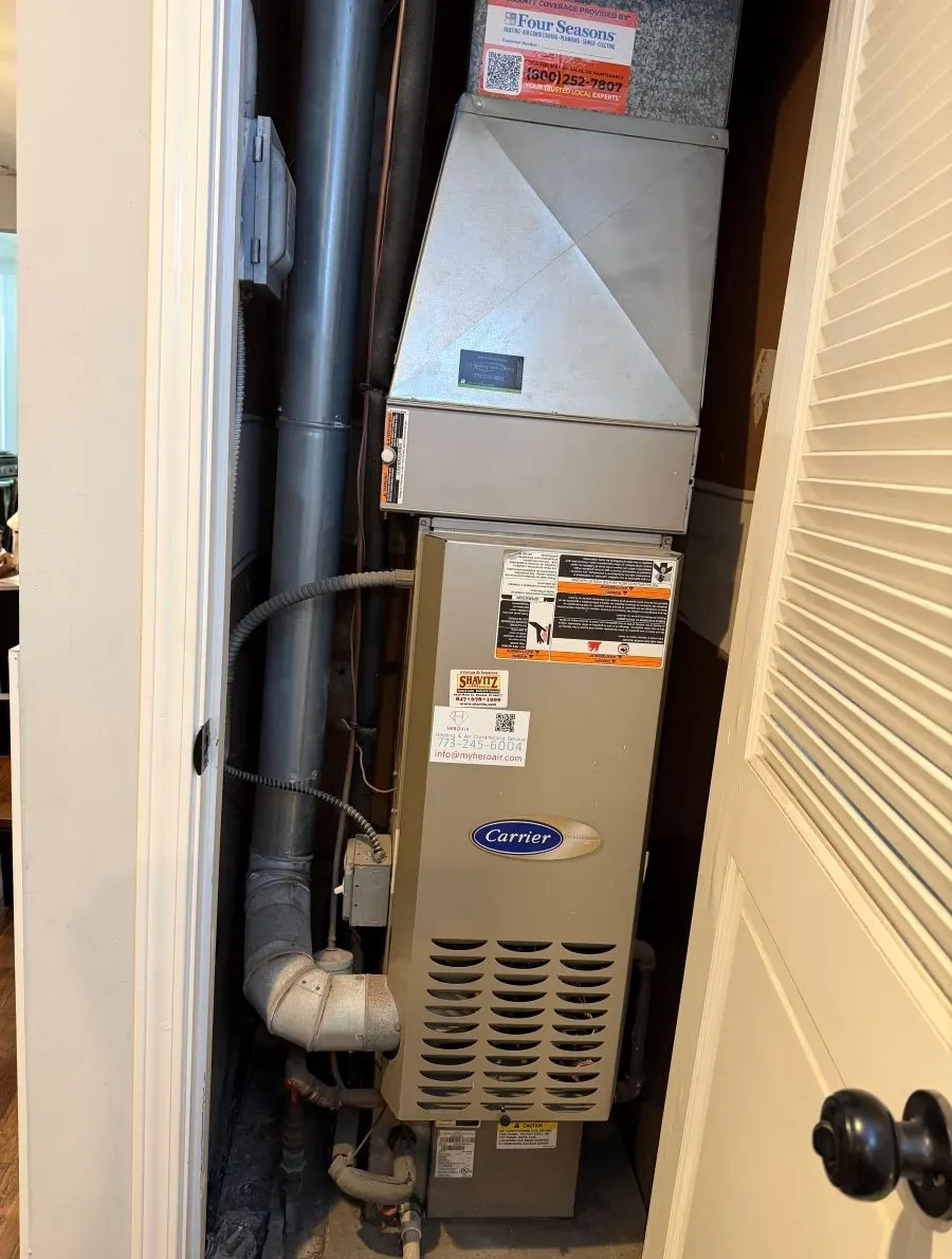 Old Carrier furnace in a hallway closet before replacement in Streamwood, Illinois by Pure Comfort Heating & Cooling